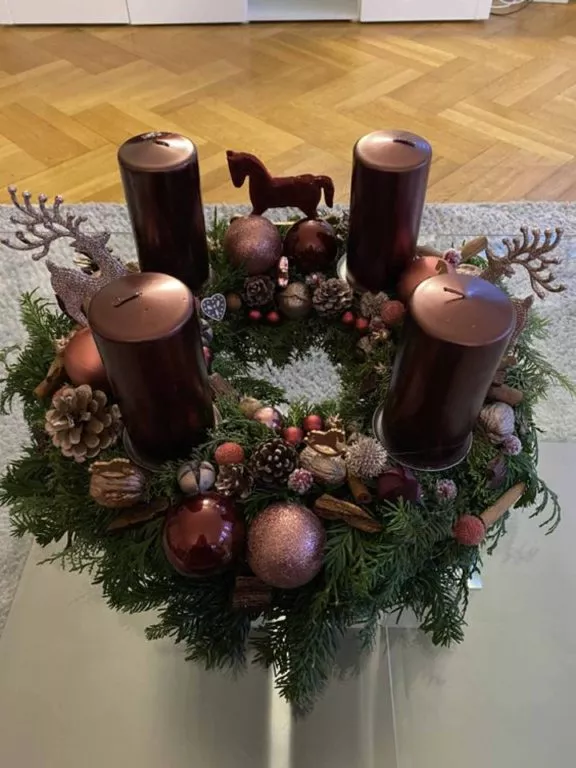 Wieniec adwentowy w ciemnej kolorystyce , brązowe świece , orzechy , szyszki , bombki. Duża ilość dodatków w wieńcu adwentowym.